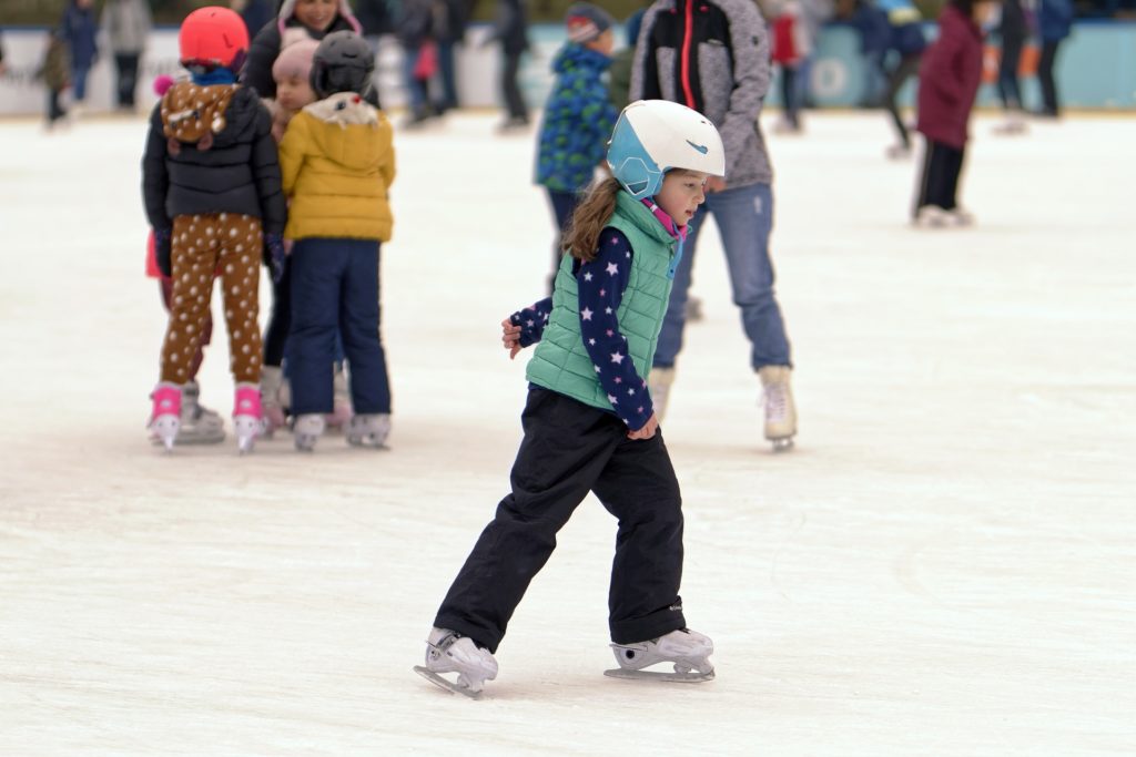 A young girl skating on an open-air ice skating rink.