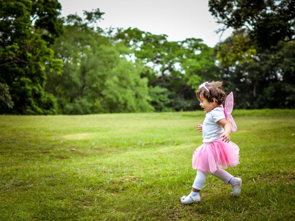 A small girl in a tutu and pink fairy wings running across a grassy field.