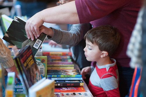 A child with a parent staring at a table of books at a local book fair.