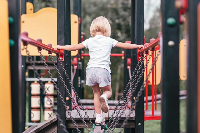 A young girl walking across a chain bridge on a local playground play-set.
