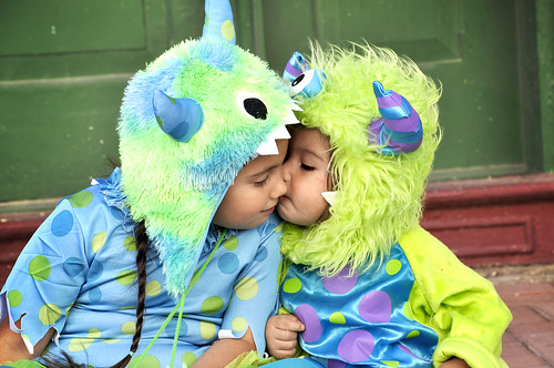 Two infant siblings, in monster costumes, sitting on a front porch.