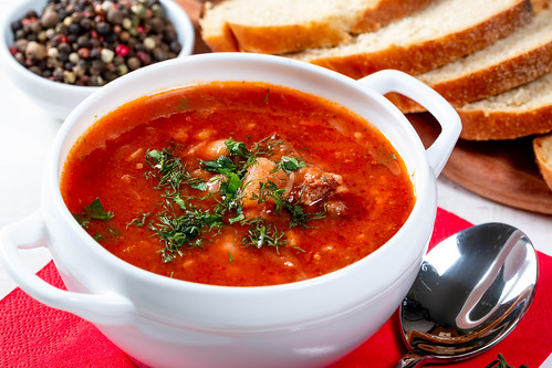 A white bowl containing traditional Ukranian soup borsch on a table with bread and a small bowl of whole peppercorns.
