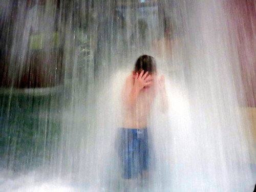 A young boy standing under a waterfall feature at a local water park.