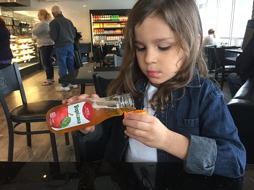A small girl pouring herself some apple juice from a bottle at a restaurant.