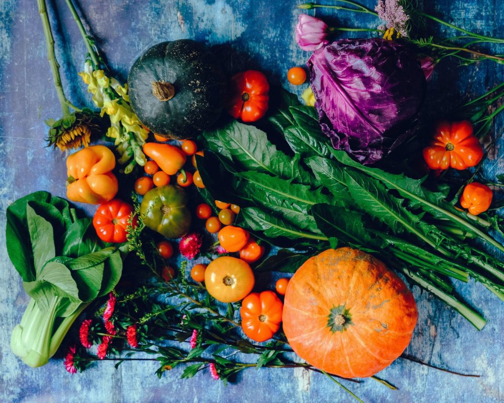 A table full of fresh green, orange, and red vegetables and gourds.