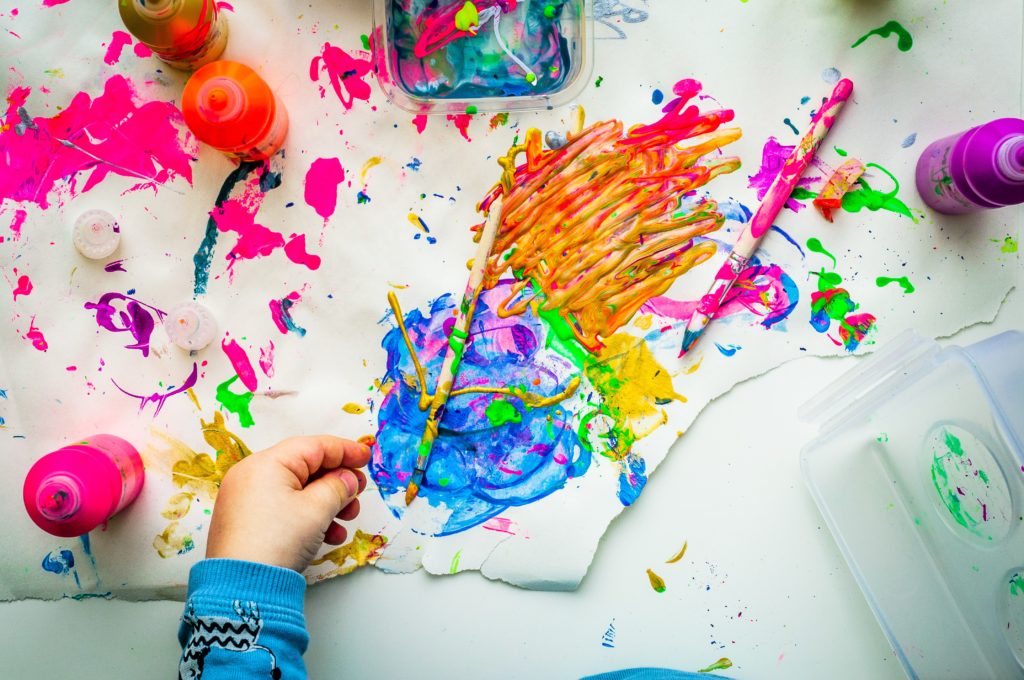 A table space where a child has been expressing their artistic creativity with acrylic paints, brushes and fingers.