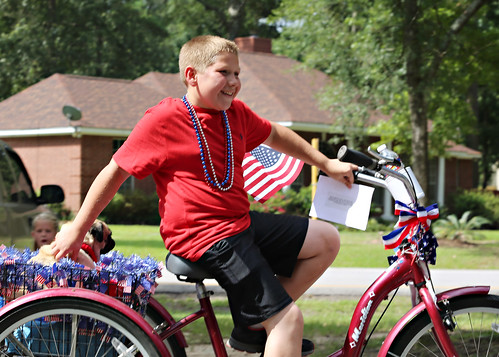 A boy riding his decorated bike down the street during an independence day parade.