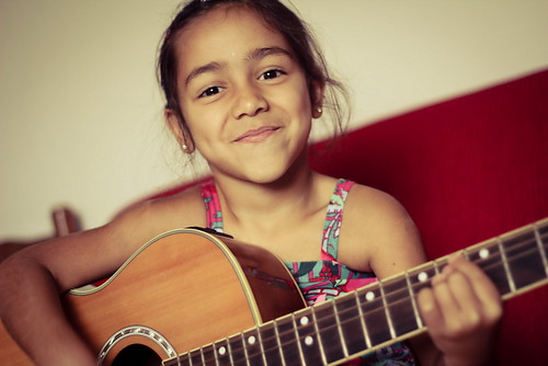 A young girl playing the guitar while sitting on a couch.