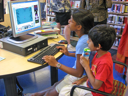 Two siblings working at a computer in their local library.