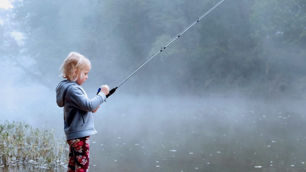 A small girl fishing on the side of a foggy river around McKinney, TX.