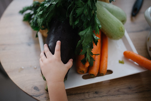 A small child's hand reaching for several vegetables laying on a table.