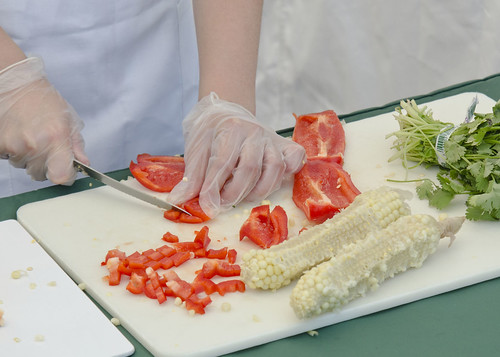 A kitchen cutting board with parsley, shaved corn cobs, and diced tomatoes.