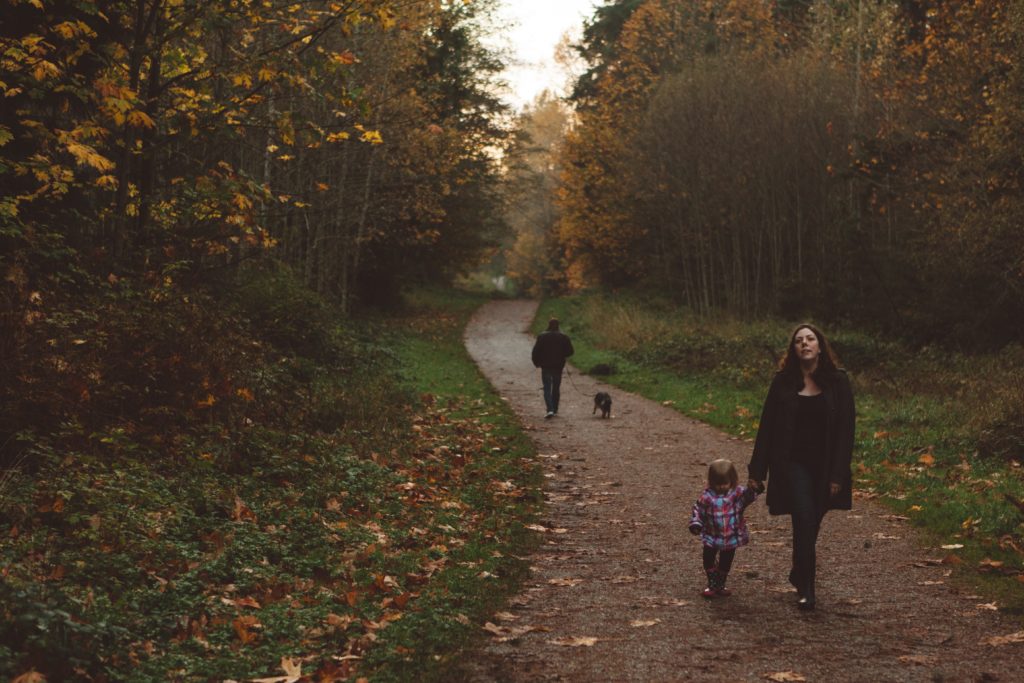 A woman walking her small daughter down a forrest trail during the fall.