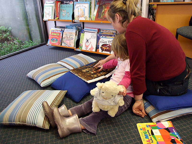 A young girl enjoying reading time their local library with her mom.