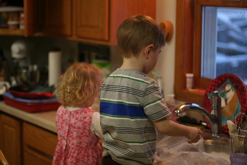 A brother and sister at the sink, helping to wash dishes.