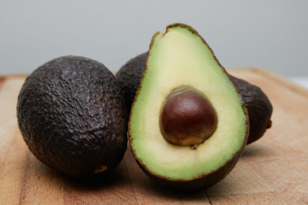 Several avocados, one sliced in half, resting on a wooden cutting board