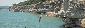 Friends jumping off a rock formation into beautiful Lake Travis outside Austin, TX.