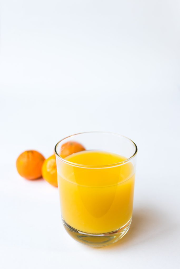 A freshly squeezed glass of Orang Juice with 3 small oranges in the background.
