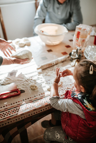 A small girl making cookies at the dining room table with her family.