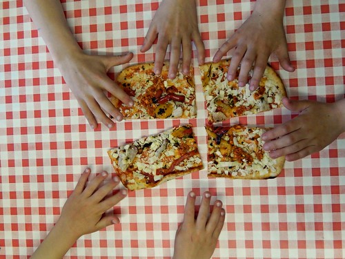 six hands reaching in to grab a piece of pizza on a red and white checkered tablecloth.