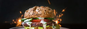 A beautifully crafted burger with fresh toppings in front of sparklers signaling an epic celebration.