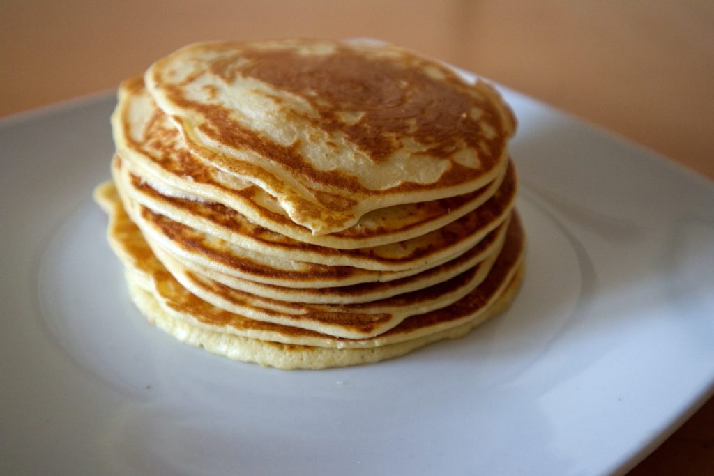 A large stack of perfectly cooked pancakes on a white ceramic plate.