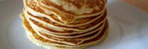 A large stack of perfectly cooked pancakes on a white ceramic plate.