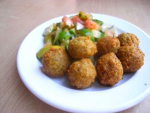 A white ceramic plate with perfectly fried Falafel balls and a vibrant Greek salad.