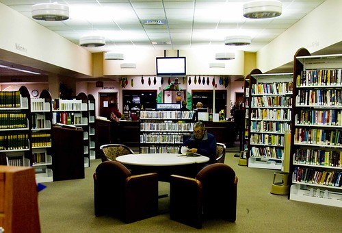 A view of the inside of a local library with a man reading at one of the tables.