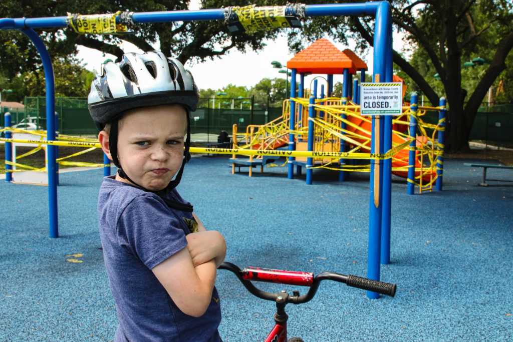 An upset boy on his bike in front of a closed off playground.