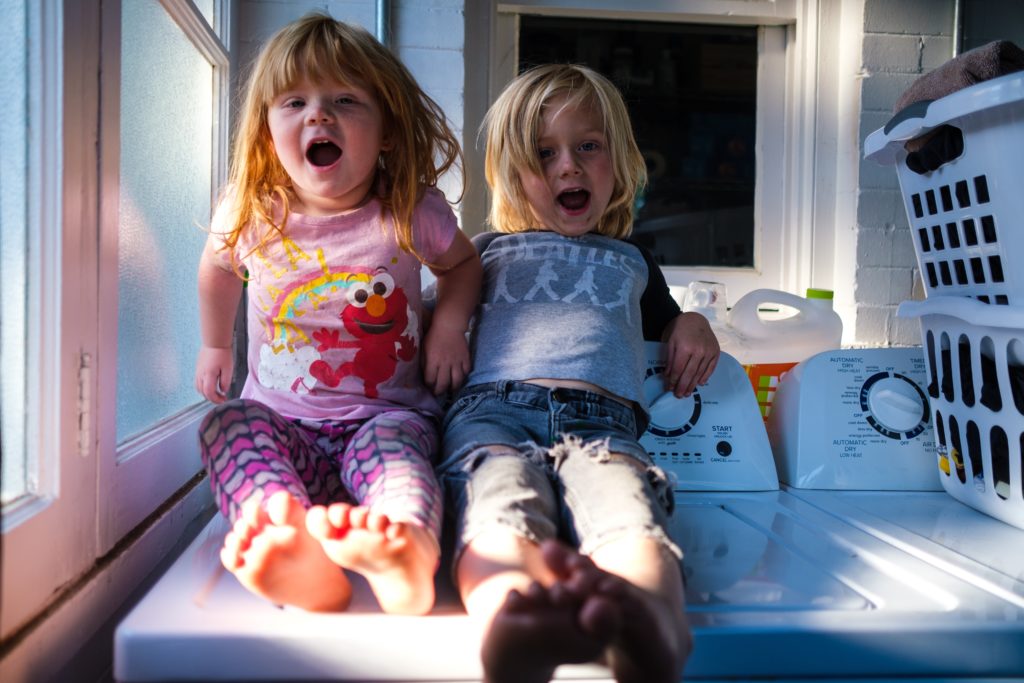 Two kids sit on the washing machine as their parents teach them about laundry