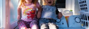Two kids sit on the washing machine as their parents teach them about laundry