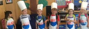 Six children in aprons and chief's hats together at a cooking camp.