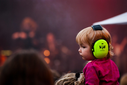 An infant enjoying a concert on the shoulders of their parent while wearing hearing protection suitable for small children.