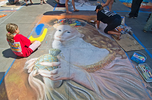 A child watches a woman create a chalk drawing at Chalkfest in Maple Grove, MN