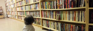 A child sitting on the floor looking at a bookshelf at a bookstore in Chicago, IL