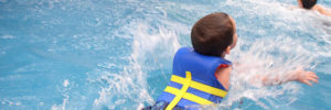 A young boy swims in a pool with his lifejacket