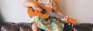 A young girl sits on the couch with a cowgirl hat playing the ukelele