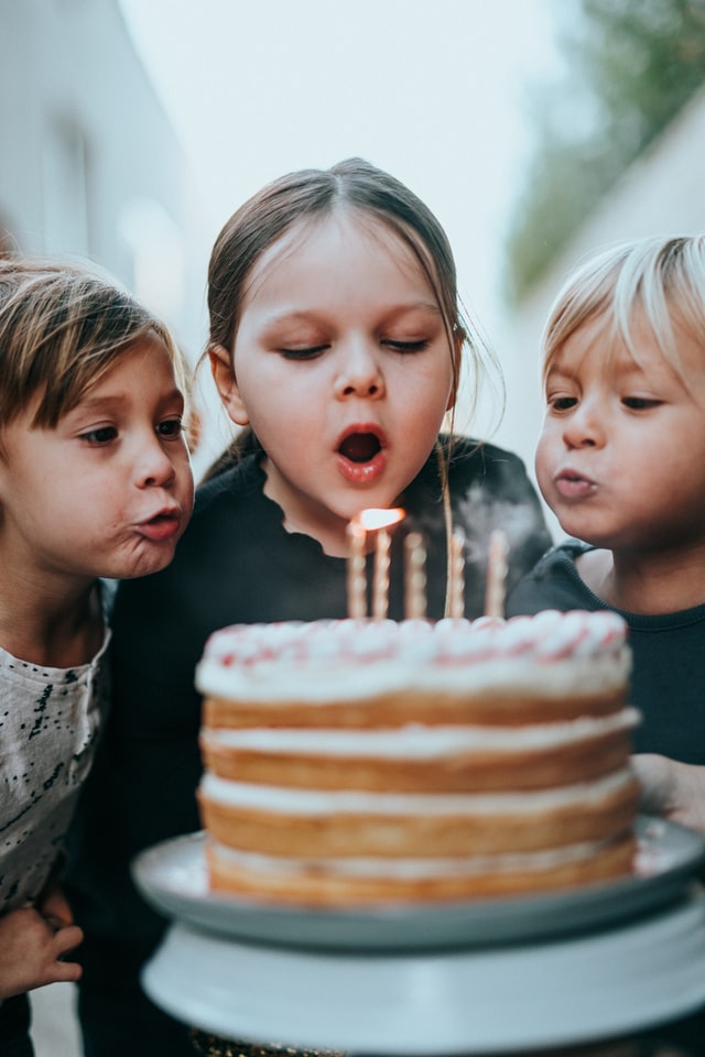Three kids blow out the candles on a birthday cake at a party venue near Gilbert, AZ
