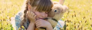 A girl lays in a field with her stuffed animal teddy bear