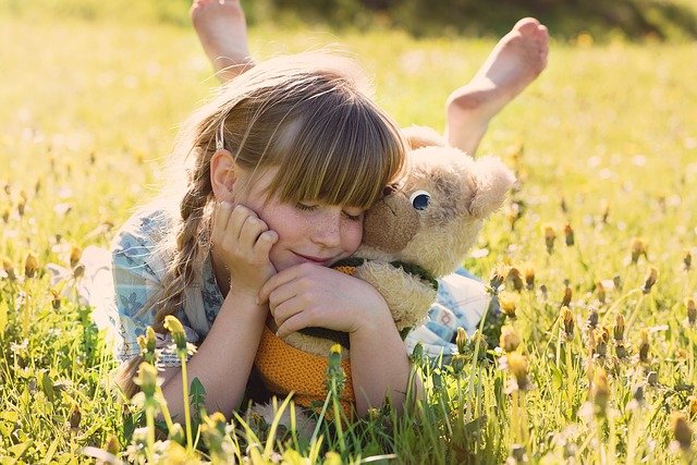 A girl lays in a field with her stuffed animal teddy bear