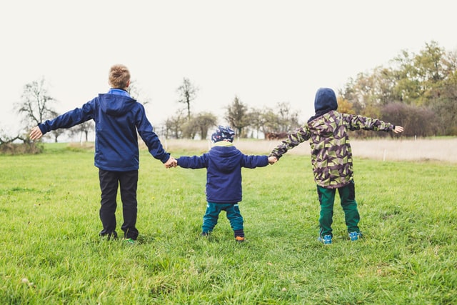 Three children hold hands at a park reserve in Maple Grove, Minnesota