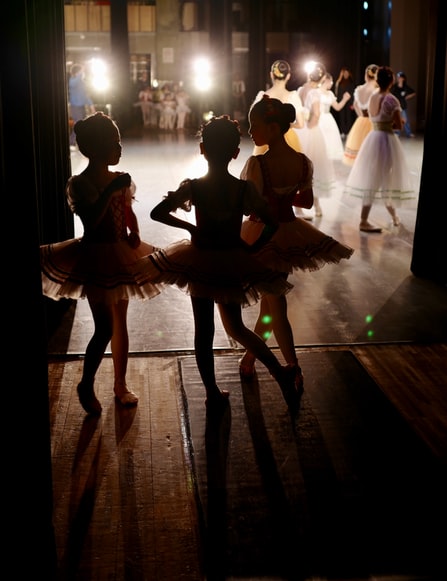 Three girls look onto the stage before a ballerina performance.