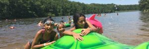 Two girls hanging onto a turtle water float in a busy river.