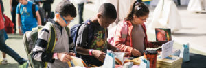 Three children looking over products at a book fair.