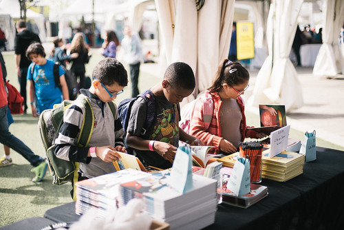 Three children looking over products at a book fair.