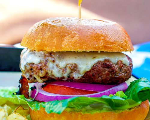 Image of a huge burger with white cheese and lots of veggies.