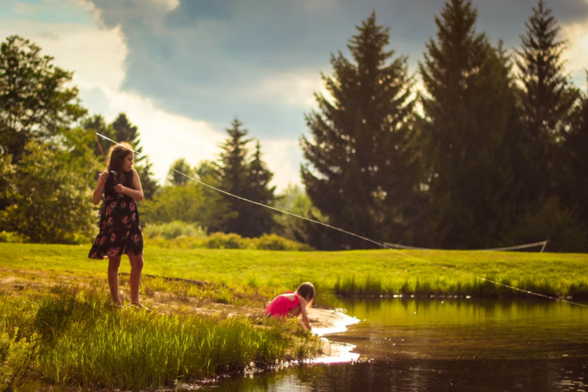Landscape shot of two girls by a pond fishing.