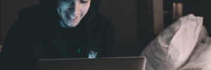Young man stares smiling at an Apple brand computer.