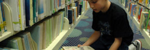 Image of a small boy reading a book on the floor of a library.